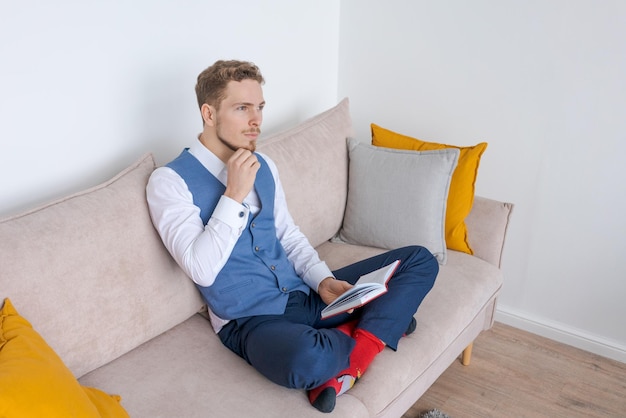 Pensive businessman sits on sofa with diary in his hand thinks about plans