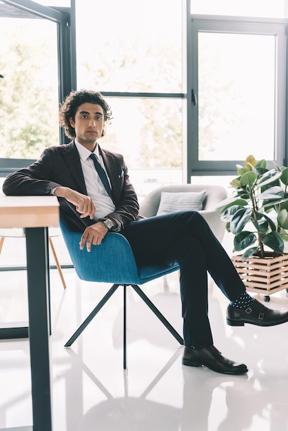 Pensive businessman in suit sitting on chair in light office