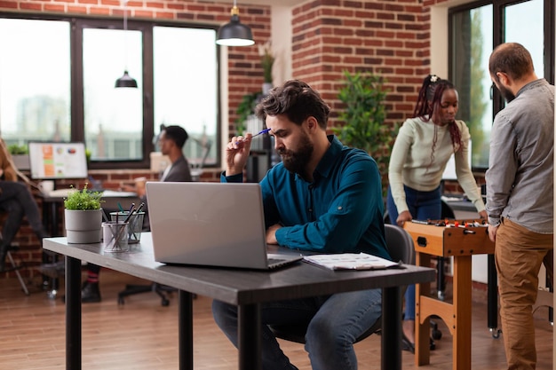 Pensive executive manager having doubtful think about marketing project analyzing company turnover on computer. Businessman working at business collaboration in startup office. Diverse team