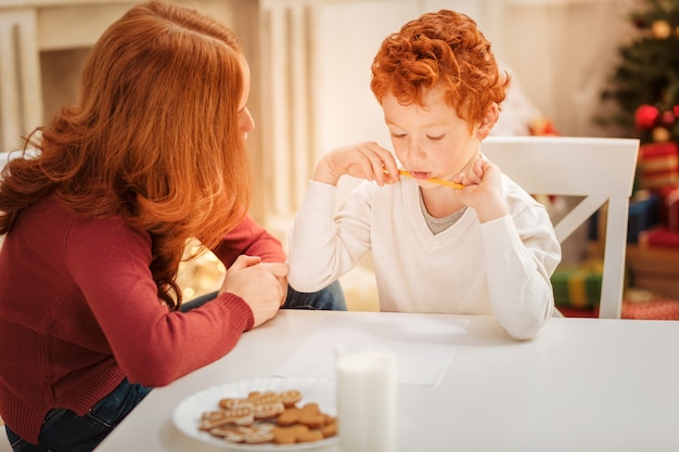 Pensive family reuniting at a dinner table while making a list of Christmas presents and writing a letter to Santa Claus.