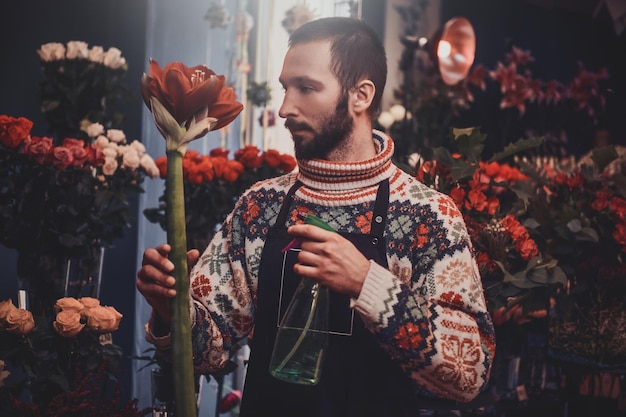 Pensive florist is posing for photographer with flower in hand at flower shop.