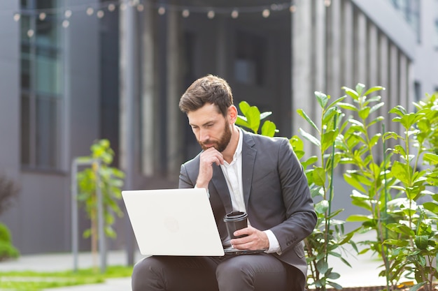 Pensive and focused male businessman working remotely at computer before making a difficult decision sitting near office before job interview