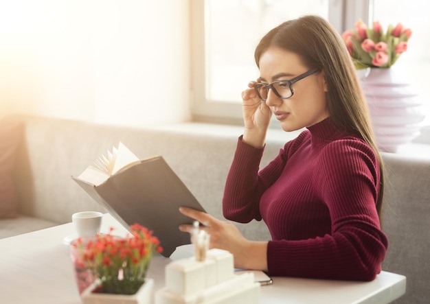 Pensive girl reading book at cafe table. Young woman having rest