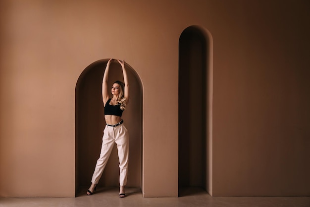 A pensive girl with a beautiful figure stands in a suit in an arch with raised arms.