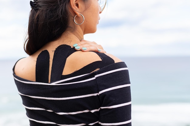 Pensive Hispanic woman touching painful shoulder on seashore