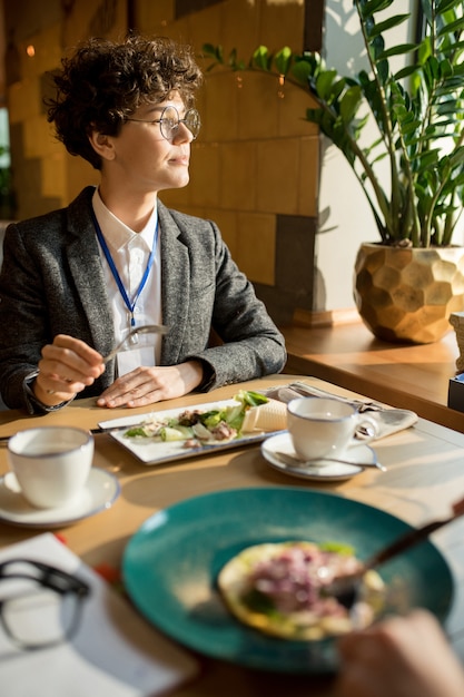 Pensive intelligent business lady eating salad in cafe