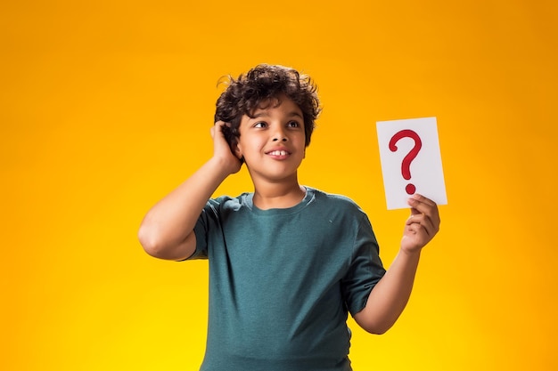 Pensive kid boy holding question mark card in hand Education and curiosity concept