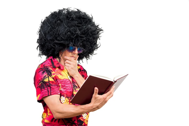 Pensive man in Afro wig and sunglasses rubbing chin and reading interesting book against white background