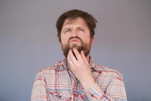 Pensive man with beard has clever expression looks thoughtfully aside