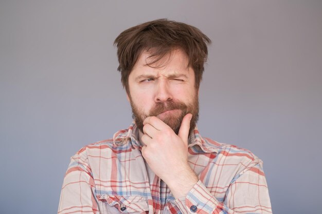 Pensive man with beard has clever expression looks thoughtfully aside