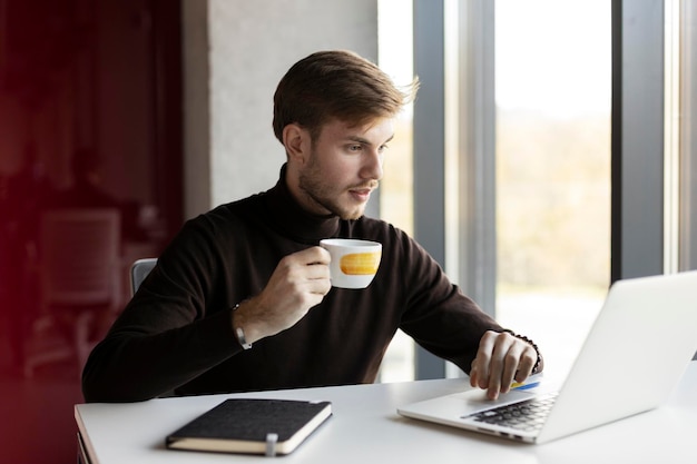 Pensive man works in the office holds a cup works on a laptop Business concept