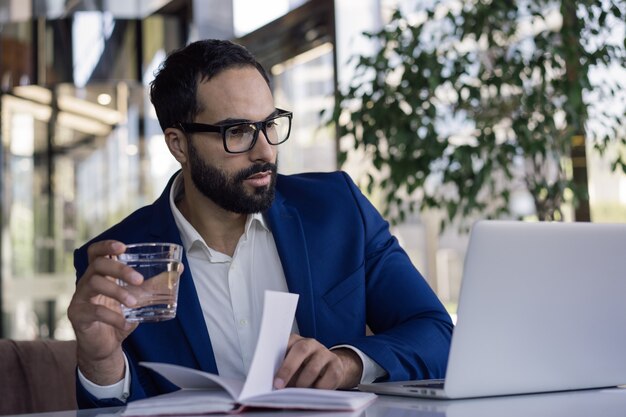 Pensive middle eastern businessman using laptop watching training courses working online in office