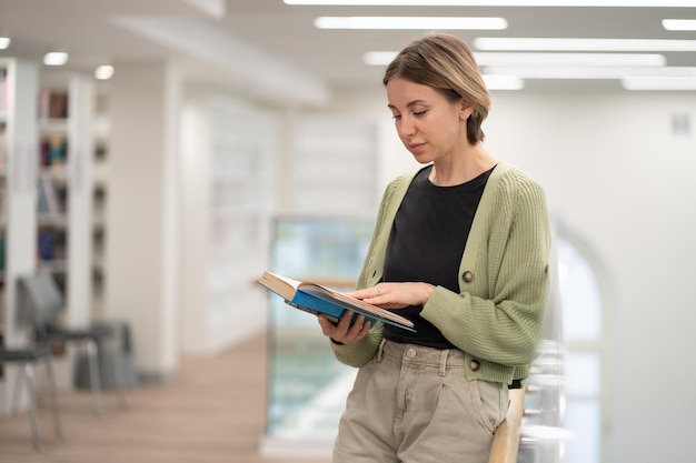 Pensive middleaged woman literature fan with paper book in hands spending leisure time in library