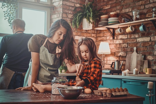 Pensive mother and her little daughter are cooking something together at the kitchen.