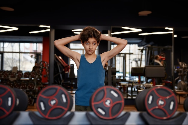 Pensive overwhelmed preteen boy looking at dumbbells having hard choice