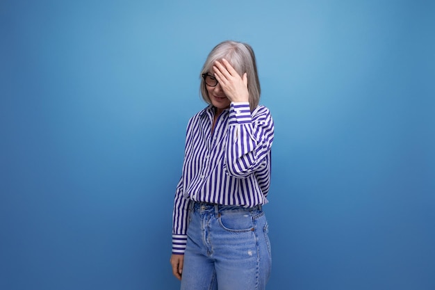 Pensive s woman with gray hair in a stylish look holding her head on a bright studio background with