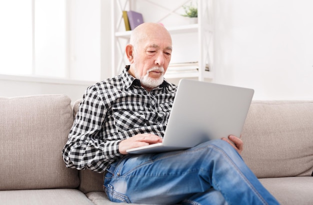 Pensive senior man reading news on laptop. Cheerful excited mature male using portable computer at home, copy space