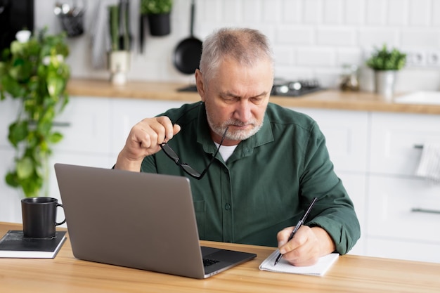 Pensive serious elderly man with laptop sitting at table check finances at home