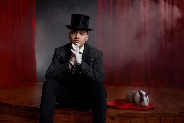 Pensive showman in suit sitting on theatre stage resting after magic show