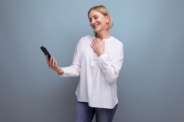 Pensive slender blondie middleaged woman in a white blouse masters the smartphone gadget