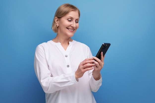 Pensive slender blondie middleaged woman in a white blouse masters the smartphone gadget