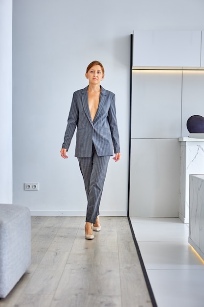 Pensive slim woman stands in room in shirtless suit