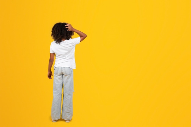 Pensive teenage black girl in white tshirt scratches head with hand isolated on yellow background