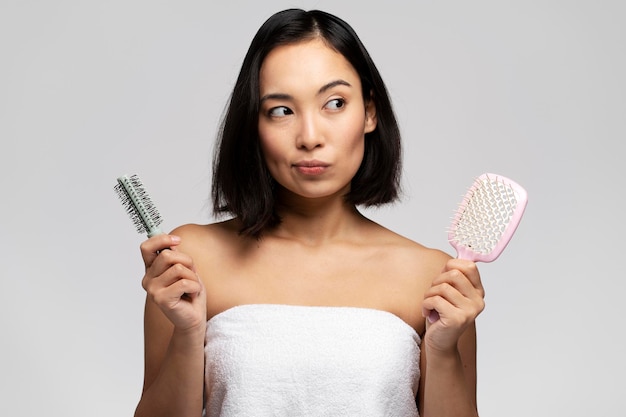 Pensive woman pondering with two hair combs while posing