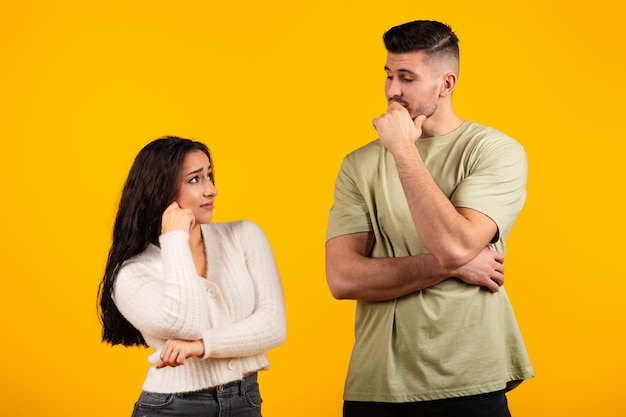 Pensive young arabic woman and guy in casual think together isolated on yellow background studio