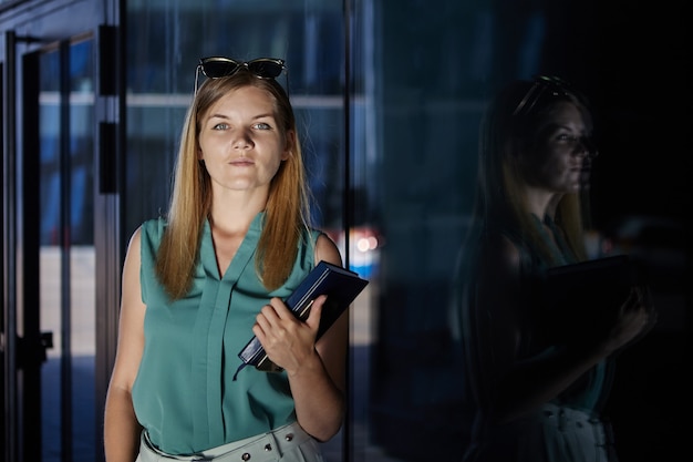 Pensive young beautiful woman with note book stands indoors