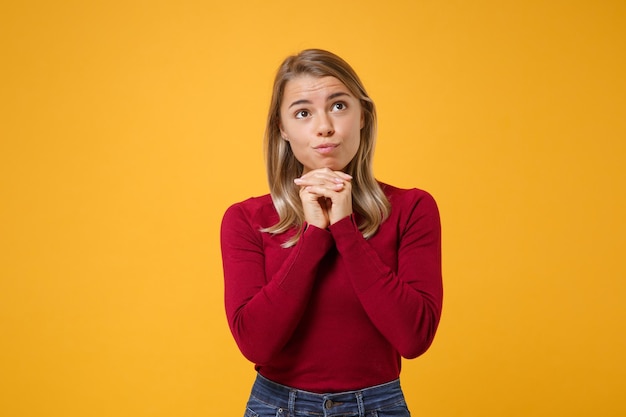 Pensive young blonde woman girl in casual clothes posing isolated on yellow orange background studio portrait. People sincere emotions lifestyle concept. Mock up copy space. Put hands prop up on chin.