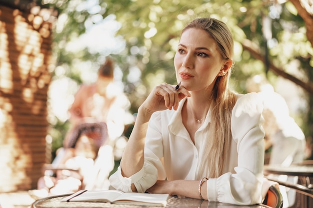 Pensive young businesswoman sitting in outdoor cafe and making notes