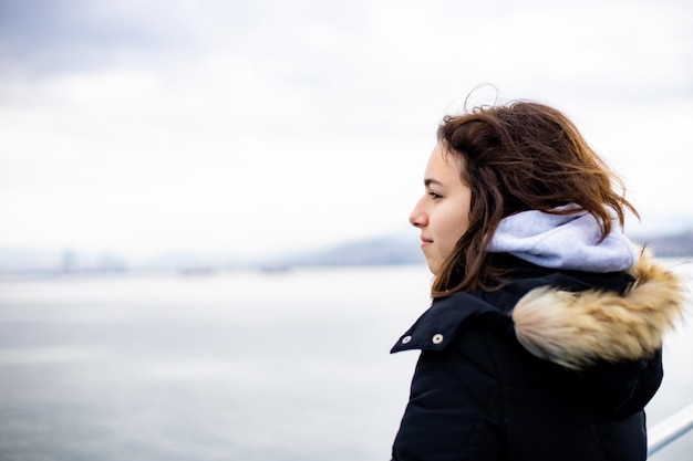 Pensive young girl looking to the sea from boat Teenager girl at ferryboat Cold grey sea