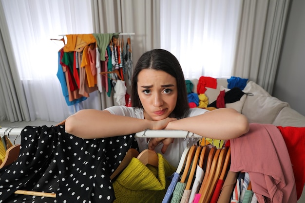 Pensive young woman with lots of clothes in room Fast fashion