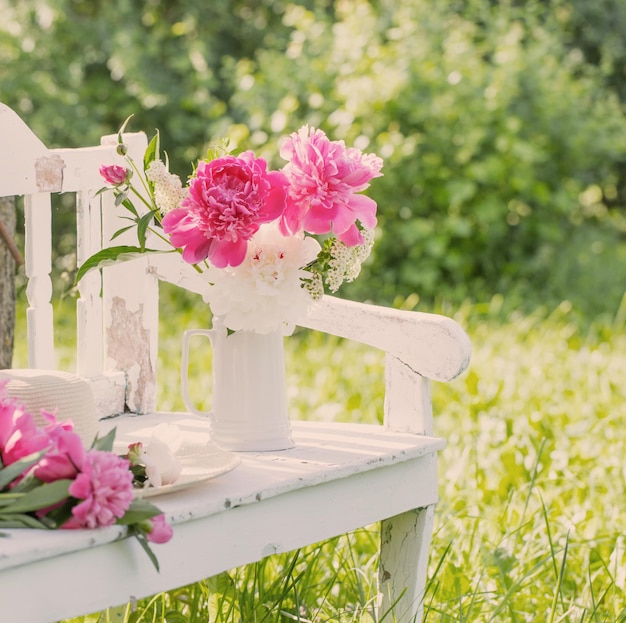 peony in jug on white wooden bench in summer garden