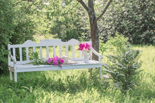 Peony in jug on white wooden bench in summer garden