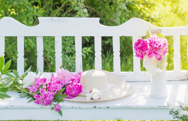 Peony in jug on white wooden bench in summer garden