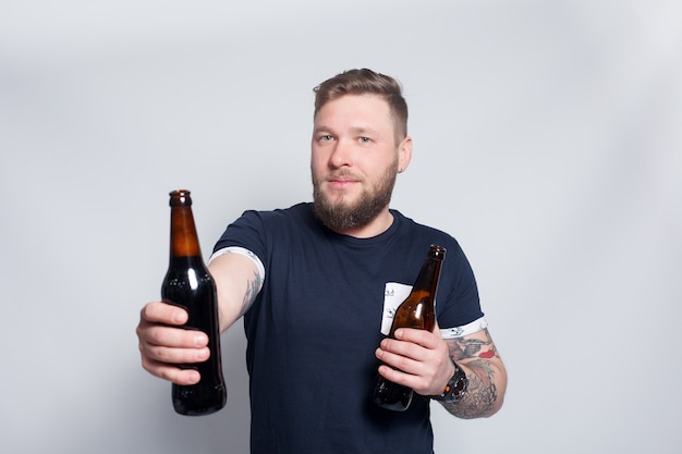 People, 4K and lifestyle concept - Brutal bearded male with tattooed arm drinks a beer from a bottle. handsome man in hat.Brutal bearded boy with tattoo