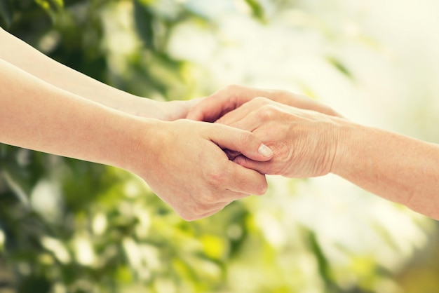 people, age, family, care and support concept - close up of senior woman and young woman holding hands over green natural background