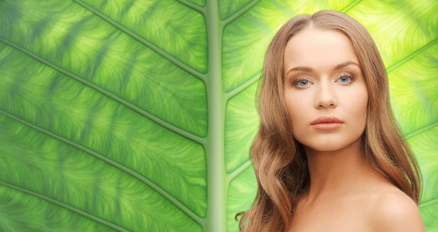 people, beauty and hair care concept - beautiful woman face with long blond hair over green natural background