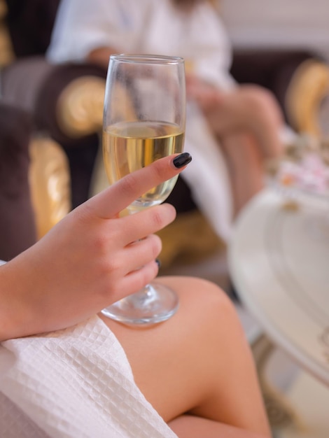 People beauty lifestyle holidays and relaxation concept beautiful young woman in white bath robe lying on chaiselongue and drinking champagne at spa