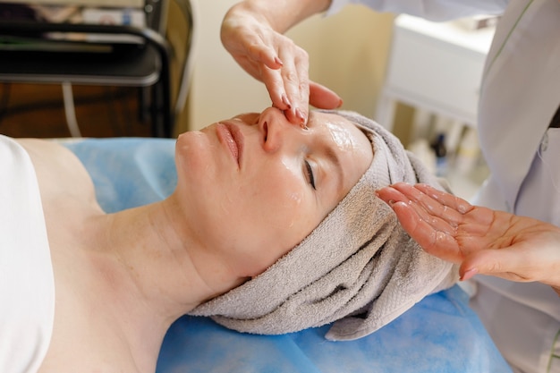 People, beauty, spa, cosmetology and technology concept - Beautiful young woman receiving facial massage with closed eyes in a spa salon