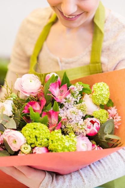 people, business, sale and floristry concept - close up of happy smiling florist woman holding bunch of flowers wrapped into paper at flower shop