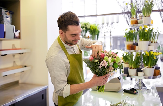 people, business, sale and floristry concept - happy smiling florist man making bunch at flower shop