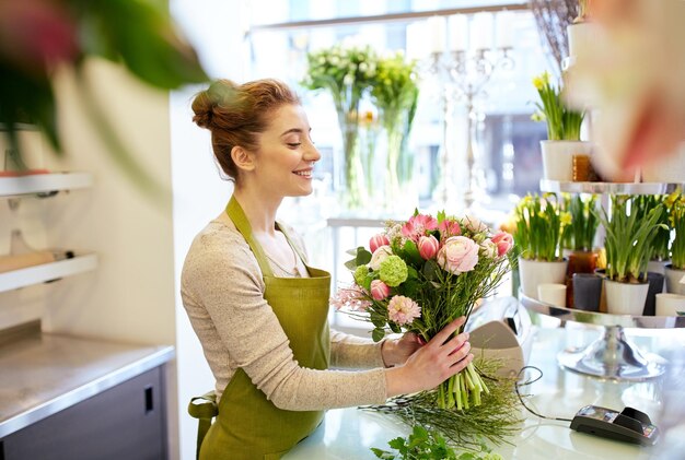 people, business, sale and floristry concept - happy smiling florist woman making bunch at flower shop