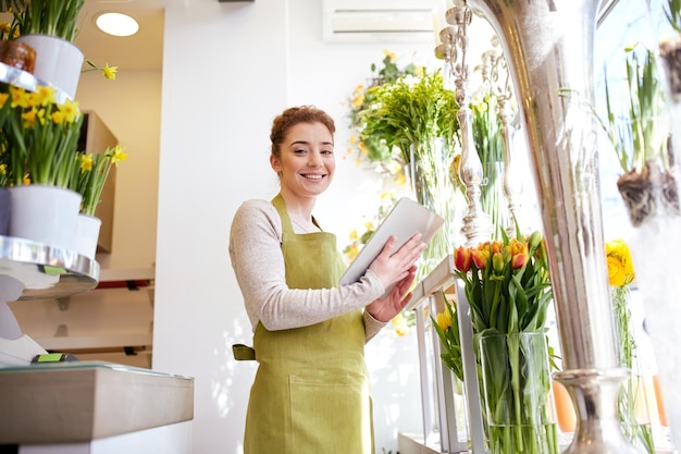 people, business, technology, sale and floristry and concept - happy smiling florist woman with tablet pc computer at flower shop