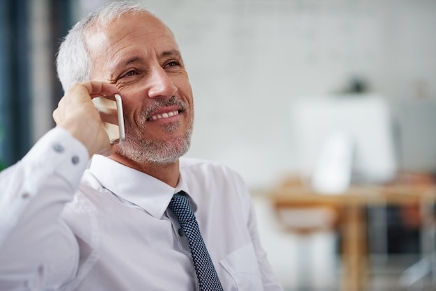 People call him for business advise Shot of a smiling mature businessman talking on a cellphone while working in an office