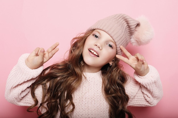 People childhood and fashion concept little girl child wearing pink winter hat and sweater over pink background