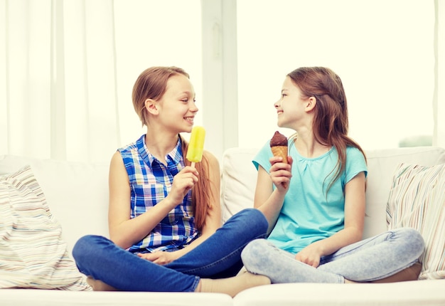 people, children, friends and friendship concept - happy little girls eating ice-cream at home