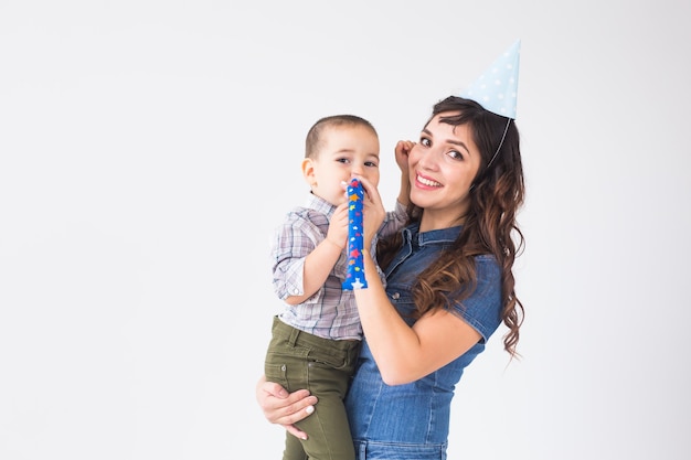 People, children and holiday concept - Charming mother hold her son wearing birthday cap over white wall with copy space.